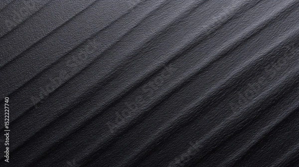 Fototapeta A dark, textured surface with a gradient of light and shadow showcases diagonal ridges creating a subtle pattern across the horizontal plane of the image.