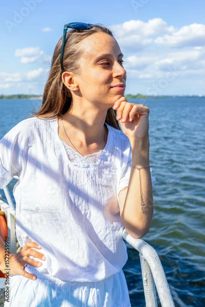 Obraz Young woman in white shirt enjoying a sunny day by the water with a thoughtful expression