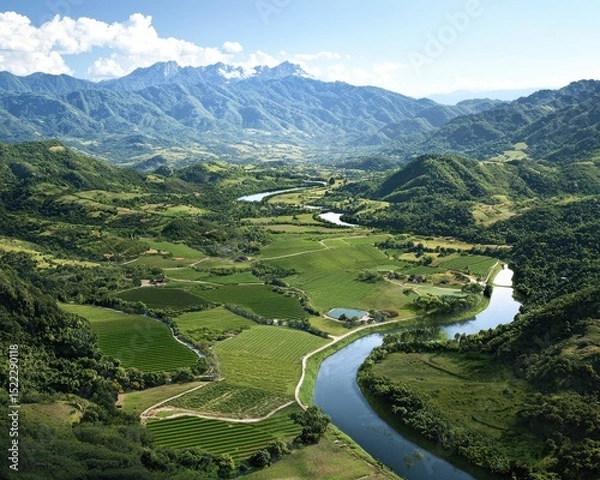 Fototapeta A lush green valley with terraced fields and a winding river, surrounded by forested hills and distant mountains under a partly cloudy sky.
