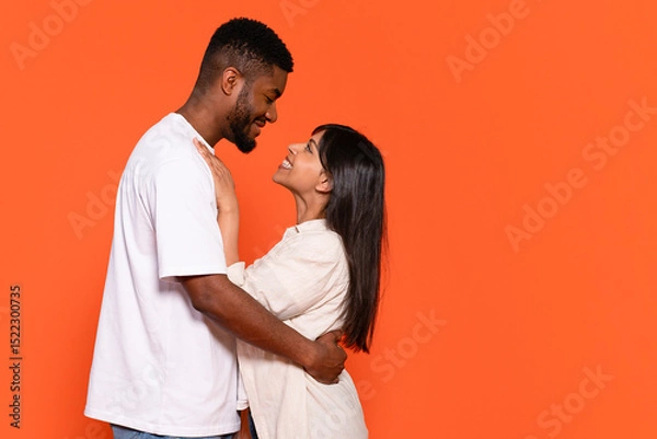 Obraz Happy couple sharing a loving moment in front of an orange background, expressing joy and affection during a casual indoor setting