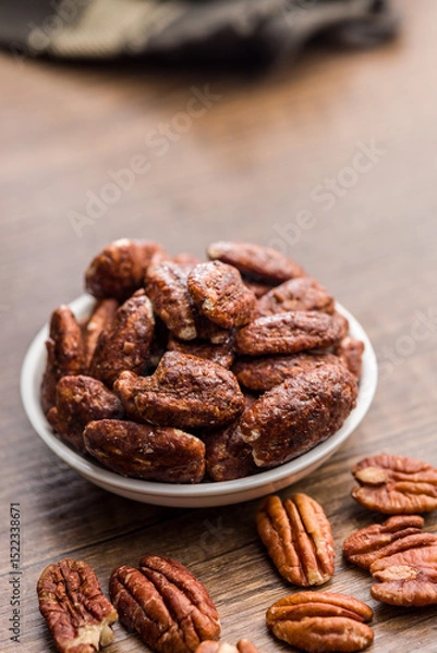 Fototapeta Pecan nuts coated in sugar and honey in bowl on wooden table.