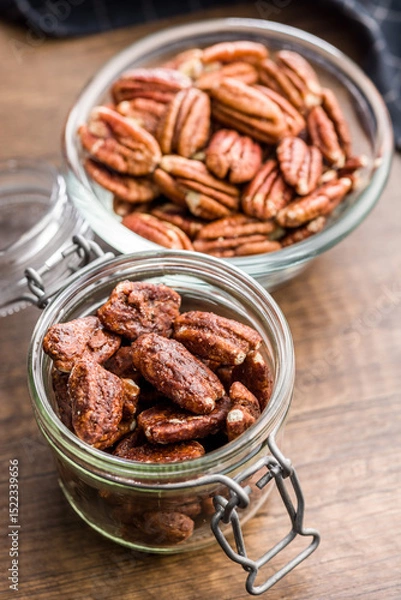 Fototapeta Pecan nuts coated in sugar and honey in jar on wooden table.