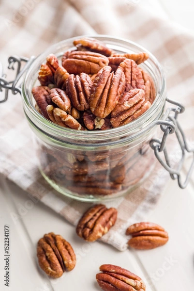 Fototapeta Peeled pecan nuts in jar on white table.