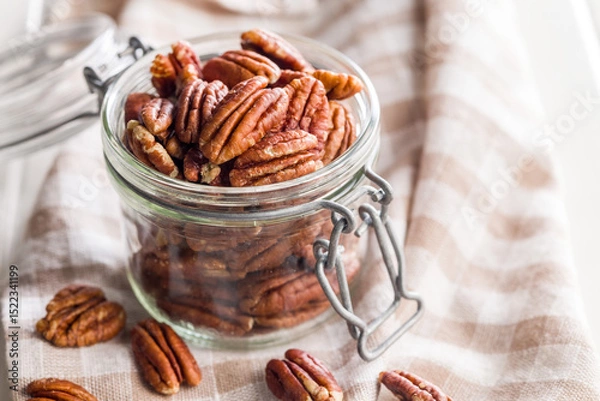 Fototapeta Peeled pecan nuts in jar on white table.