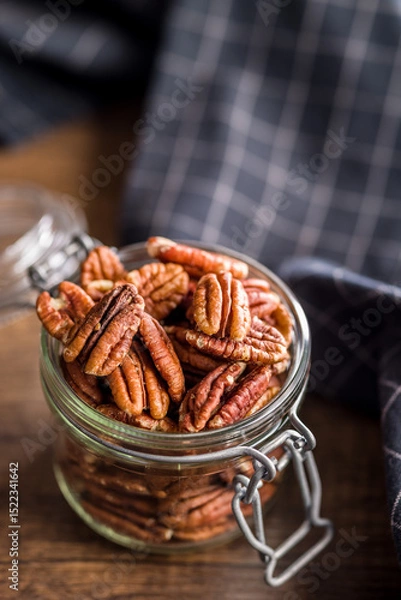 Fototapeta Peeled pecan nuts in jar on wooden table.