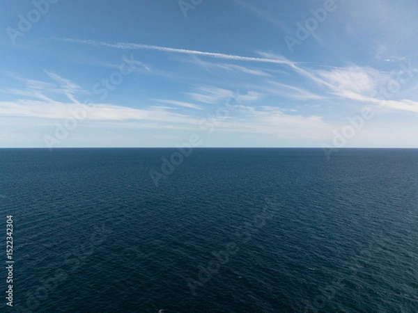 Fototapeta A serene view of the blue ocean stretching to the horizon under a bright and cloud-streaked sky. Thailand, Koh Tao.