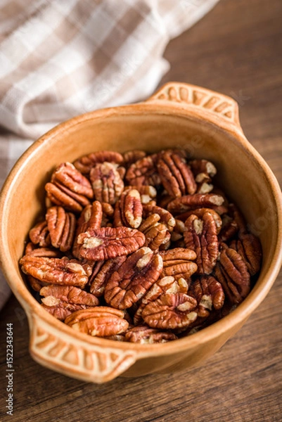 Fototapeta Peeled pecan nuts in bowl on wooden table.