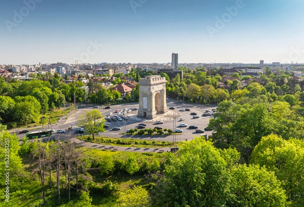 Fototapeta Arch of Triumph in Bucharest aerial photo. Travel to Bucharest Romania. Aerial view over this amazing historical landmark from Romania during a summer day with green parks landscape.