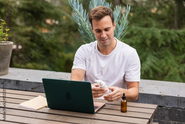 Fototapeta Man buying body products online using laptop in garden