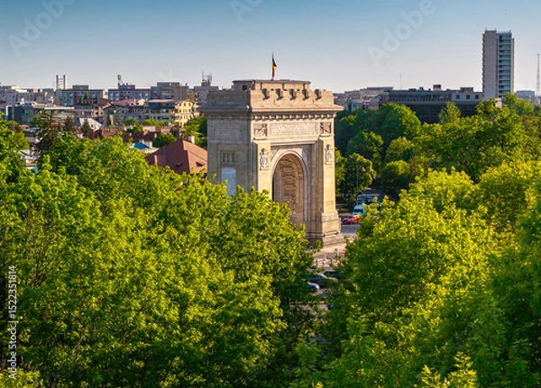 Fototapeta Arch of Triumph in Bucharest aerial photo. Travel to Bucharest Romania. Aerial view over this amazing historical landmark from Romania during a summer day with green parks landscape.