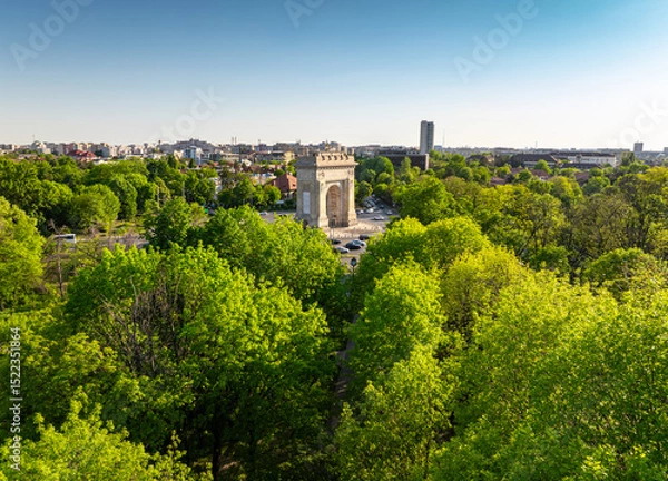Fototapeta Arch of Triumph in Bucharest aerial photo. Travel to Bucharest Romania. Aerial view over this amazing historical landmark from Romania during a summer day with green parks landscape.