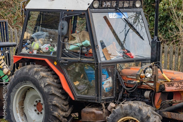 Obraz A tractor with a cabin full of junk stands in the yard of a family farm