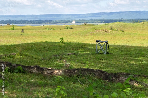 Fototapeta Relaxing camping chair set under tree shade on a beautiful grassy meadow. Ideal for outdoor, travel, and nature-themed concepts. Peaceful, natural setting for lifestyle imagery.