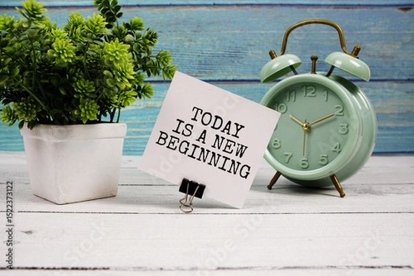 Fototapeta Today is a new beginning  text written on paper card with alarm clock on wooden background