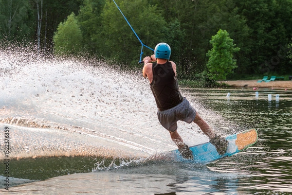 Obraz Wakeboarder making tricks. Low angle shot of man wakeboarding on a lake. Man water skiing at sunset.
