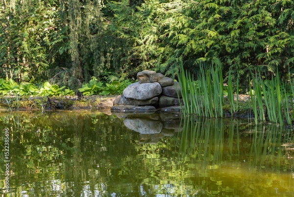 Fototapeta Tranquil pond with stacked rocks and lush greenery, reflecting serene natural beauty. Nature concept for spring design.