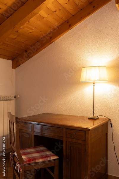 Fototapeta Detail of a corner of a bedroom with a desk a chair and a lamp with a light on. Everything looks old