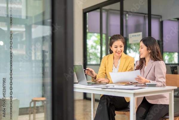 Obraz Two professional businesswomen are working on laptop computers sitting at desks in the office. Colleagues are happy and discussing the digital strategy of the Graph