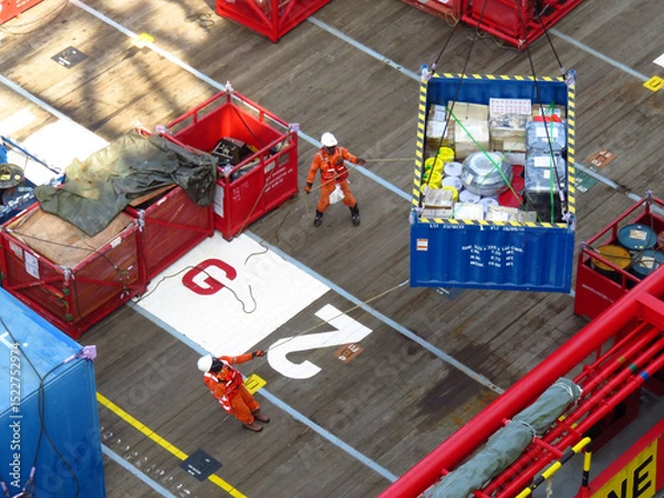 Obraz Workers expertly maneuver a heavy cargo container across a ships deck using ropes and precision. The scene showcases meticulous teamwork and efficient cargo handling procedures aboard a vessel.