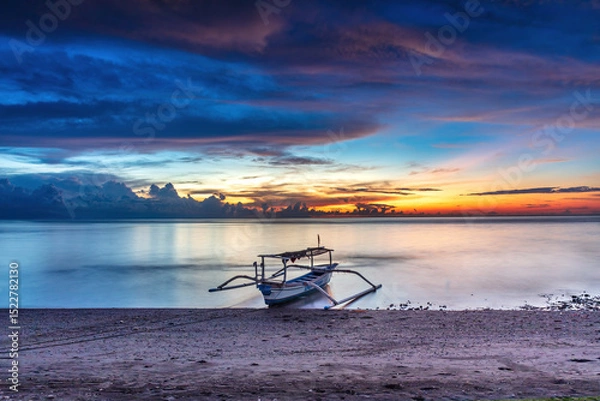 Obraz Ocean sunset at Lovina Beach, northern Bali, Indonesia. Beach with boat in theforeground; setting sun surrounded by colorful clouds. Sun's reflection on the water. 
