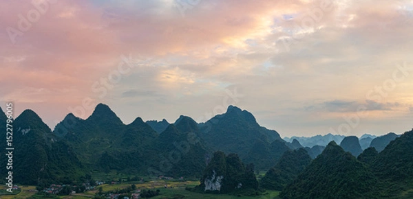 Obraz A breathtaking aerial view of a dramatic sunrise illuminating the sky with vibrant orange and red hues over mist-covered karst mountains. The serene landscape, dotted with valleys and rivers,