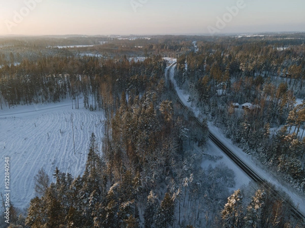 Fototapeta A road  winds through a snowy forest, where frosty trees