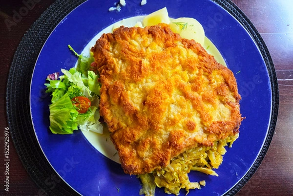 Fototapeta Crispy Breaded Schnitzel with Fresh Salad and Savory Cabbage on a Blue Plate