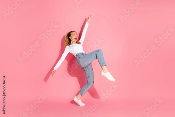 Fototapeta Young female in casual style dancing joyfully on a vibrant pink background wearing fashionable attire and showcasing happiness and energy