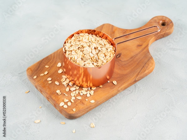 Fototapeta Rolled oats in measuring cup on wooden board