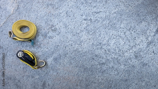 Obraz Yellow ratchet straps resting on concrete surface, securing heavy loads during transportation, highlighting professional cargo handling equipment. Copy space