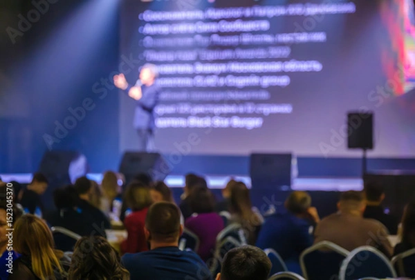 Obraz Engaging speaker presenting to attendees in a conference hall with focus on interaction.