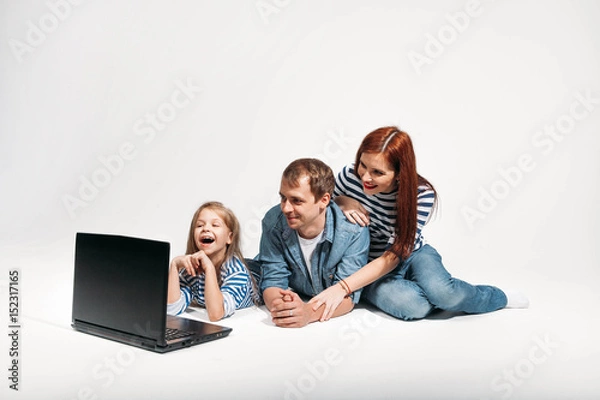Fototapeta Happy family Father, mother and child lying on the floor with laptop on white background isolated