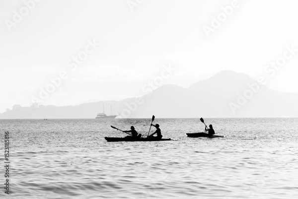 Obraz Three athletes paddling their kayaks on a cloudy day