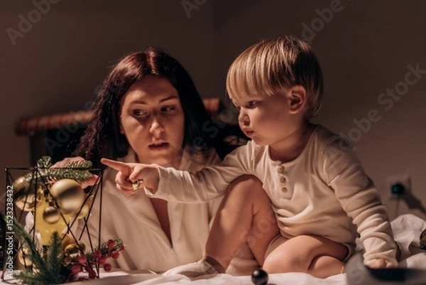 Fototapeta Curious toddler points with wonder as mother listens closely sharing a quiet moment of discovery warmth during cozy family holiday evening The atmosphere is warm and intimate, suggesting a moment