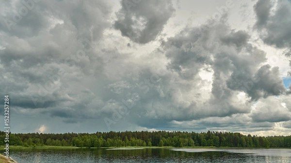 Fototapeta Grey rainy clouds over the lake. Dense forest along the lake shore during a storm.