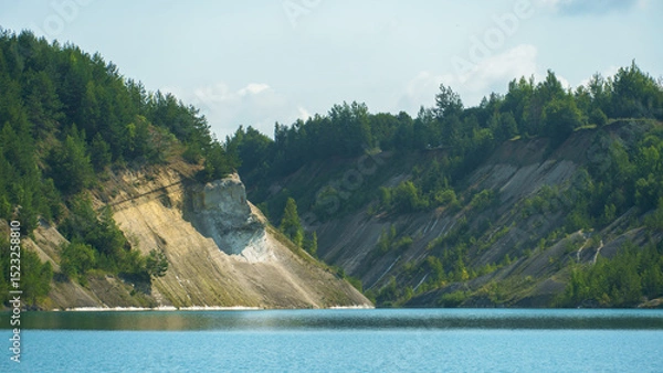 Fototapeta An old abandoned sand quarry. The shore of the quarry is overgrown with forest. Extraction of sand and stone for industrial applications.