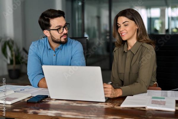 Obraz Two smiling busy professional business people working in office with laptop computer. Female executive manager talking to male colleague or partner having conversation sitting at workplace.