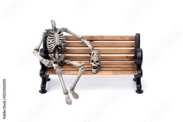Fototapeta Haunted by ghosts. Human headless skeleton sits near his skull with a ghostly face on old wooden bench isolated on white background.