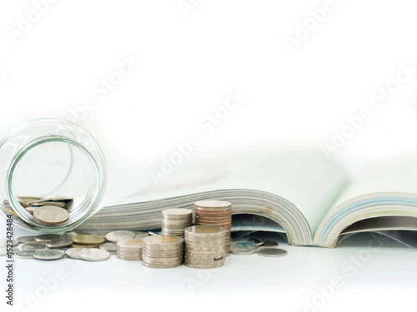 Fototapeta A coin jar and an open book are placed beside a pile of coins.