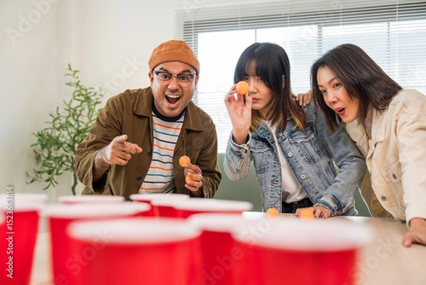 Obraz Office leisure group and board games. Happy asian diverse group friends playing together with beer ping pong at home office standing at the table enjoying time together.