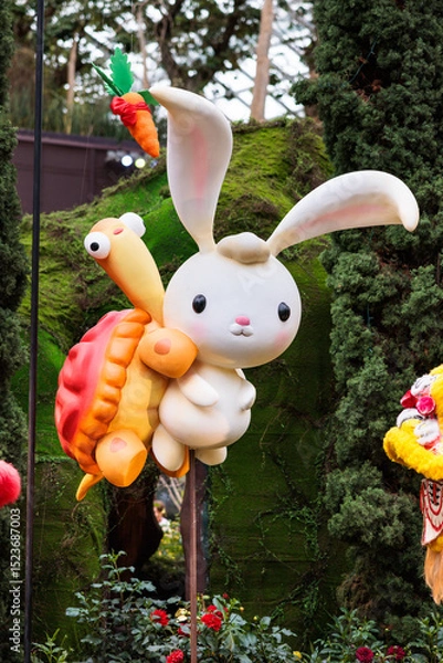 Fototapeta Cute and adorable cartoon-like rabbit and turtle emerging from flowers at gardens by the bay
