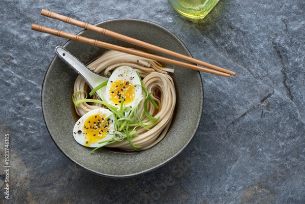 Fototapeta Bowl of miso udon with boiled egg on a dark-grey granite background, horizontal shot with space, top view