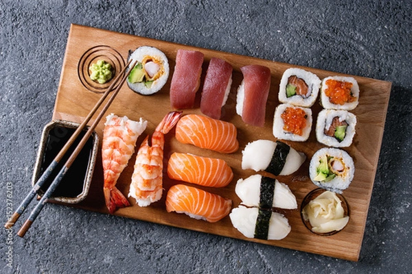 Fototapeta Sushi ustawił rolety Nigiri i sushi na drewnianej desce serwingowej z sosem sojowym i pałeczkami na tle czarnego kamiennego tekstury. Widok z góry z przestrzenią. Menu Japonii