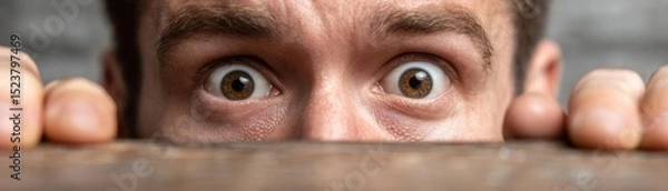 Fototapeta Panic attack by managing stress and fear concept. A close-up of a surprised man peeking over a surface.