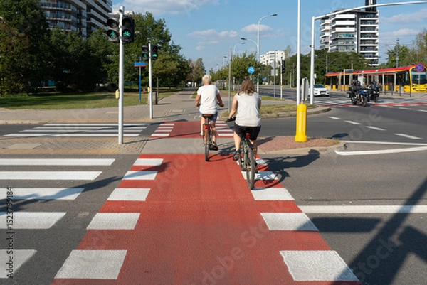 Fototapeta Cyclists ride on a dedicated red bike path in Warsaw, Poland. This illustrates modern urban mobility and the popularity of the bicycle as a sustainable form of city transport.