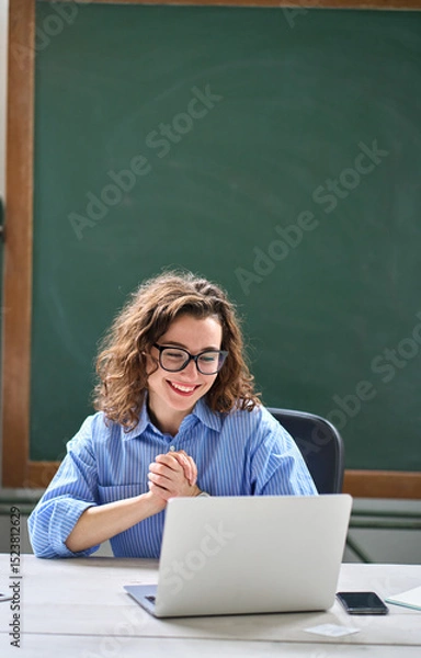 Obraz Young happy business woman employee or teacher feeling pleased and excited looking at laptop reading good news online about career growth, satisfied with great result sitting at work desk. Vertical