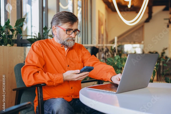 Obraz Senior Man Managing Finances with Laptop and Calculator in Modern Office