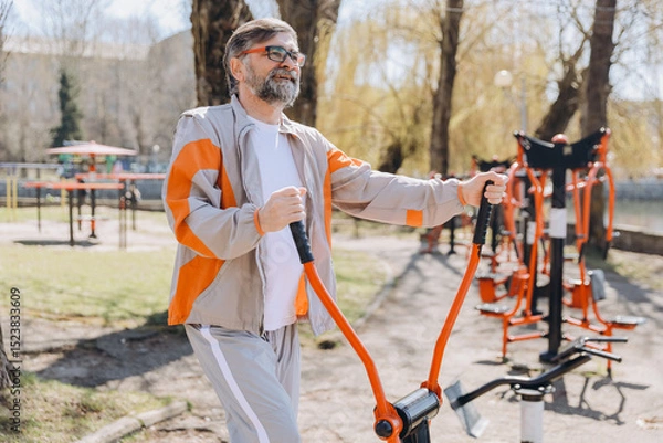 Obraz Senior man exercising on outdoor gym equipment in a park