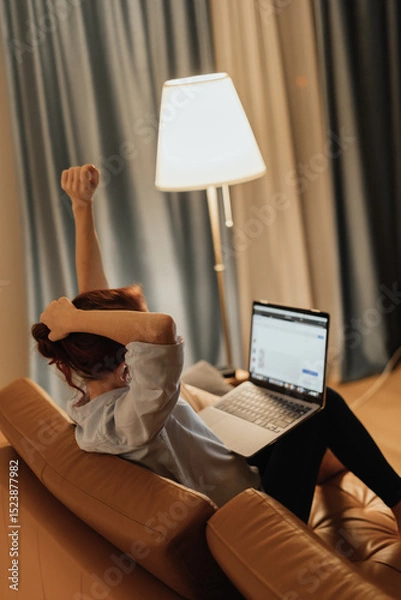 Fototapeta Woman stretches arms while working on laptop from couch symbolizing stretching at home office digital detox and remote work wellness showing importance of healthy posture habits and mindful pauses