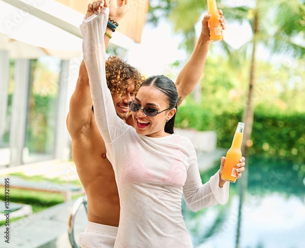 Fototapeta Young people having fun dancing and drinking and bonding listening to music at a party by pool in a villa or resort, Young people enjoying vacation in a tropical resort hotel